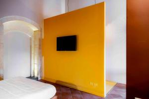 ein Schlafzimmer mit einer gelben Wand, an der ein Fernseher hängt in der Unterkunft Feudo Bauly in Palazzolo Acreide