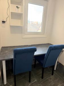 a table with two blue chairs and a window at Beni Apartman in Szeged