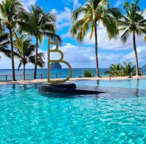a pool with a sign in the water with palm trees at Studio Calm Blue in Le Diamant