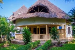 a house with a thatched roof and palm trees at Jumbo Art S Villas in Diani Beach