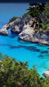 a beach with blue water and a rocky coastline at Eliseo's rooms in Triei