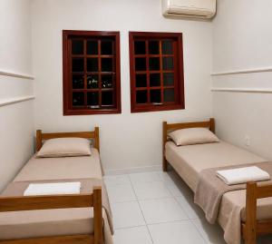 two beds in a room with two windows at Pousada Economia in Paracatu