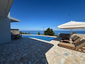 a patio with chairs and an umbrella and a swimming pool at Vento Villas in Agios Nikitas