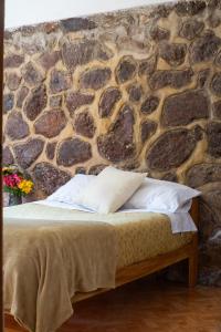 a bed in a room with a stone wall at Colibri Wasi Pisac in Cusco