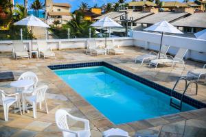 a swimming pool with white chairs and tables and a table and chairs at Pousada Capitães do Mar in Porto De Galinhas