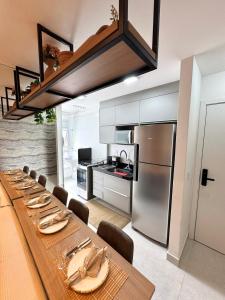 a long wooden table with chairs and a kitchen at Infinity 1206 - 2 Quartos a Passos da Praia com Garagem in Vila Velha