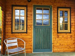 a wooden cabin with a green door and a chair at Boho Bungalow in Nelson