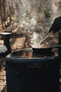 a person cooking food in a pan on a grill at Tanières MicroChalets Charlevoix in Baie-Saint-Paul