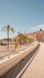 a long bench with palm trees on a beach at La Plage - Studio - Face à la Mer - Clim Terrasse in Menton +22 photos