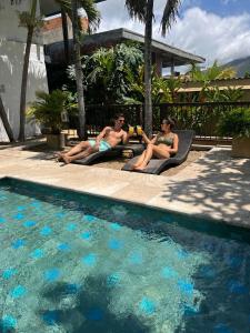 two people sitting on lounge chairs next to a swimming pool at Lombok Hotel & SPA antes Hotel Casablanca in Guaduas