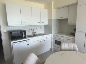 a kitchen with white cabinets and a sink and a table at Studio Zeester in Westende-Bad