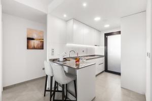 a kitchen with white cabinets and a bar with stools at Skyline Infinity Apartment Eagle Tower Benidorm in Benidorm