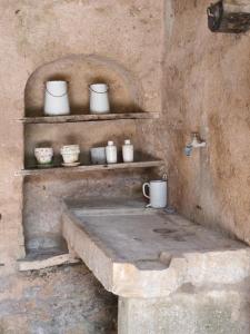 a stone kitchen with white cups and bowls on shelves at La petite maison d'à côté in Noyers