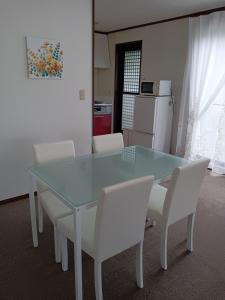 a kitchen with a glass table and white chairs at guest house mami in Taketa