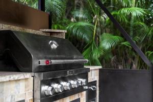 an outdoor grill in a garden with palm trees at Elegant, 4 BDR house with a pool and BBQ in Wellington
