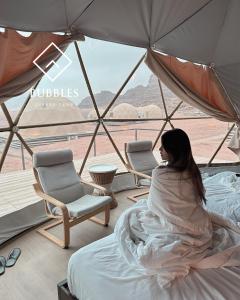 a woman sitting on a bed in a tent with a view at BUBBLES LUXURY CAMp in Wadi Rum