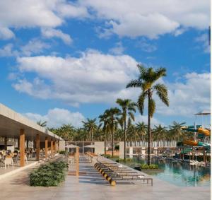 a resort with a pool and palm trees and chairs at Apartamento no Beach Resort Salinas in Ilha de Atalaia