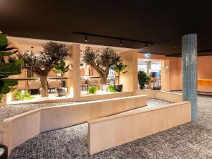 a lobby with trees and benches in a building at Novotel Macon Nord - Porte de Bourgogne in Mâcon