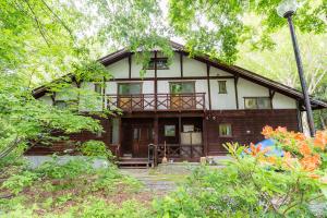 a large wooden house with a porch in the woods at Ikiru Lodge in Yamanouchi