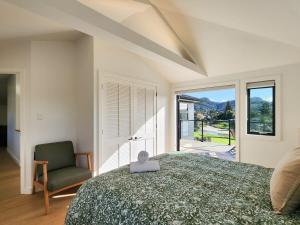a bedroom with a bed and a chair and a window at Serenity Sands Beach House in Hahei