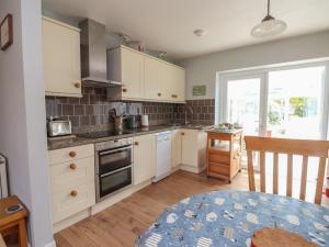 a small kitchen with white cabinets and a table at Bro Mebyd in Criccieth