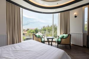 a bedroom with a bed and chairs and a large window at Can Gio Park Hotel in Cần Giờ