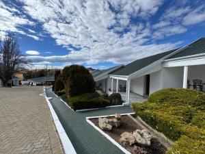 a white house with a yard with bushes and trees at Mountain Shadows Hotel in Barkly East
