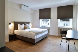 a bedroom with a bed and a table and two windows at SAXX Apartments Hagen in Hagen