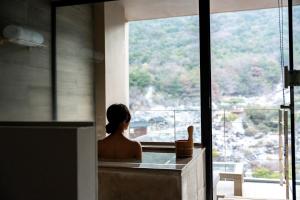 eine Frau, die in einer Badewanne sitzt und aus einem Fenster schaut in der Unterkunft Unzen Kyushu Hotel in Unzen