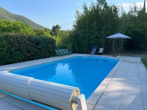 a blue swimming pool with chairs and an umbrella at Logis Sol Levante in Arles-sur-Tech