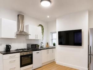 a kitchen with white cabinets and a flat screen tv at SidemerseyLivings - Step-Free 4BR Home, Ground Floor Bed & Bath, Private Gated Parking in Liverpool