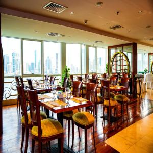 a restaurant with wooden tables and chairs and windows at Golden Tulip Sharjah in Sharjah