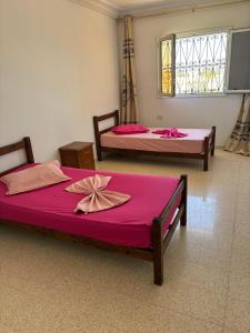 two beds in a room with pink sheets and a window at Résidence el hachen in Djerba