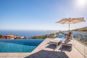 a woman sitting in a chair next to a swimming pool at Villa Platinum by Homie in Estreito da Calheta