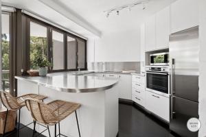 a white kitchen with a large island with two chairs at Peggy - Little Cove in Noosa Heads