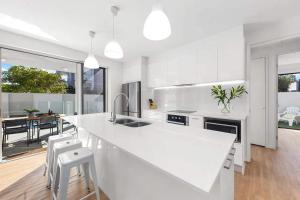 a white kitchen with a large white counter and chairs at Waves Beach House in Marcoola