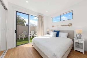 a white bedroom with a bed and a balcony at Waves Beach House in Marcoola