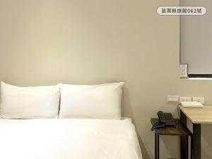 a bedroom with a bed with white sheets and a telephone at WE Hotel in Miaoli