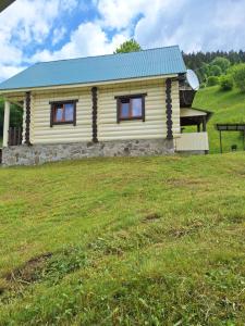 a small yellow cabin with a blue roof on a field at Лісовий котедж in Synevyrsʼka Polyana +12 photos