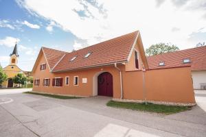 an orange building with a red door and a church at Geigenhof in Neudorf bei Ilz