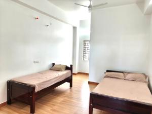 two beds in a room with white walls and wooden floors at Sekar Inn in Arumuganeri