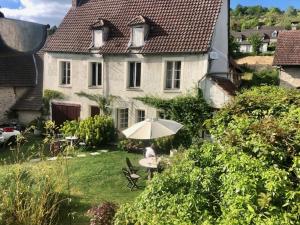 a person sitting at a table with an umbrella in front of a house at La chambre de la grenouille in Giverny +22 photos