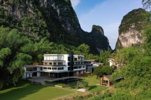 a house on a hill with mountains in the background at L'Eau Vive de Qixi Meidi - Riverfront Infinity Pool & Log Cabin Cafe - Outdoor Cooking Class - Complimentary Shuttle within 8 Kilometers in Yangshuo