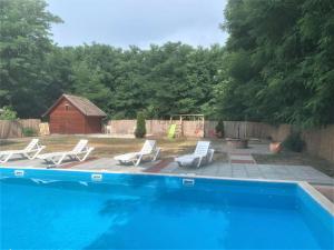 a swimming pool with white chairs and a house at CUKROS Villa in Cserkeszőlő