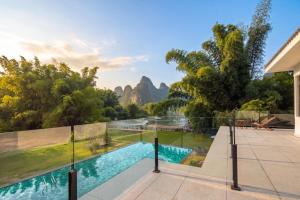 a house with a swimming pool with mountains in the background at L'Eau Vive de Qixi Meidi - Riverfront Infinity Pool & Log Cabin Cafe - Outdoor Cooking Class - Complimentary Shuttle within 8 Kilometers in Yangshuo