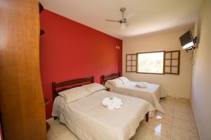 twee bedden in een kamer met een rode muur bij Pousada Luar do Sertão in Valença