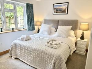 a bedroom with a bed with a white comforter and two windows at Wyndthorpe Cottage in Milton Abbas