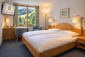 a bedroom with a bed and a desk and a window at Hotel Alpina Parpan in Parpan