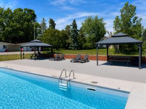 a swimming pool with two umbrellas and chairs and a table at Ramada by Wyndham 1000 Islands Gananoque in Gananoque