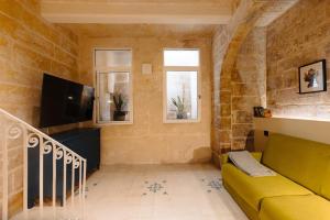 a living room with a yellow couch and a tv at Ta' Dolor - Kalkara Heritage Maisonette in Kalkara